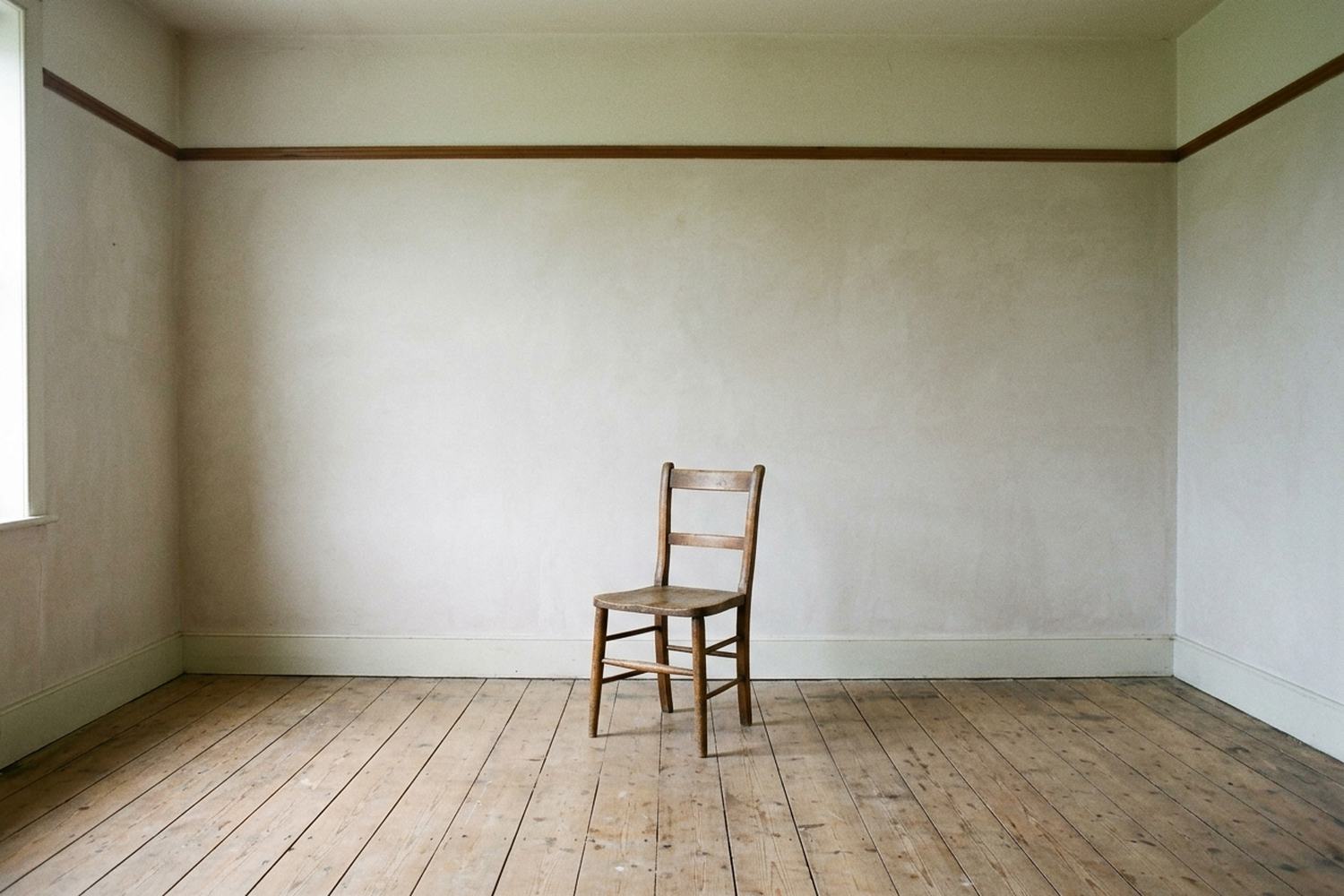 A bare room with a picture rail and one plain chair standing near the middle.