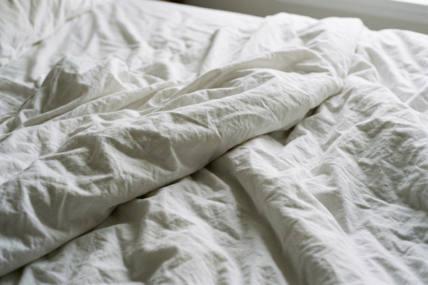 Rumpled white bed linen filling the frame, showing folds and shadow.