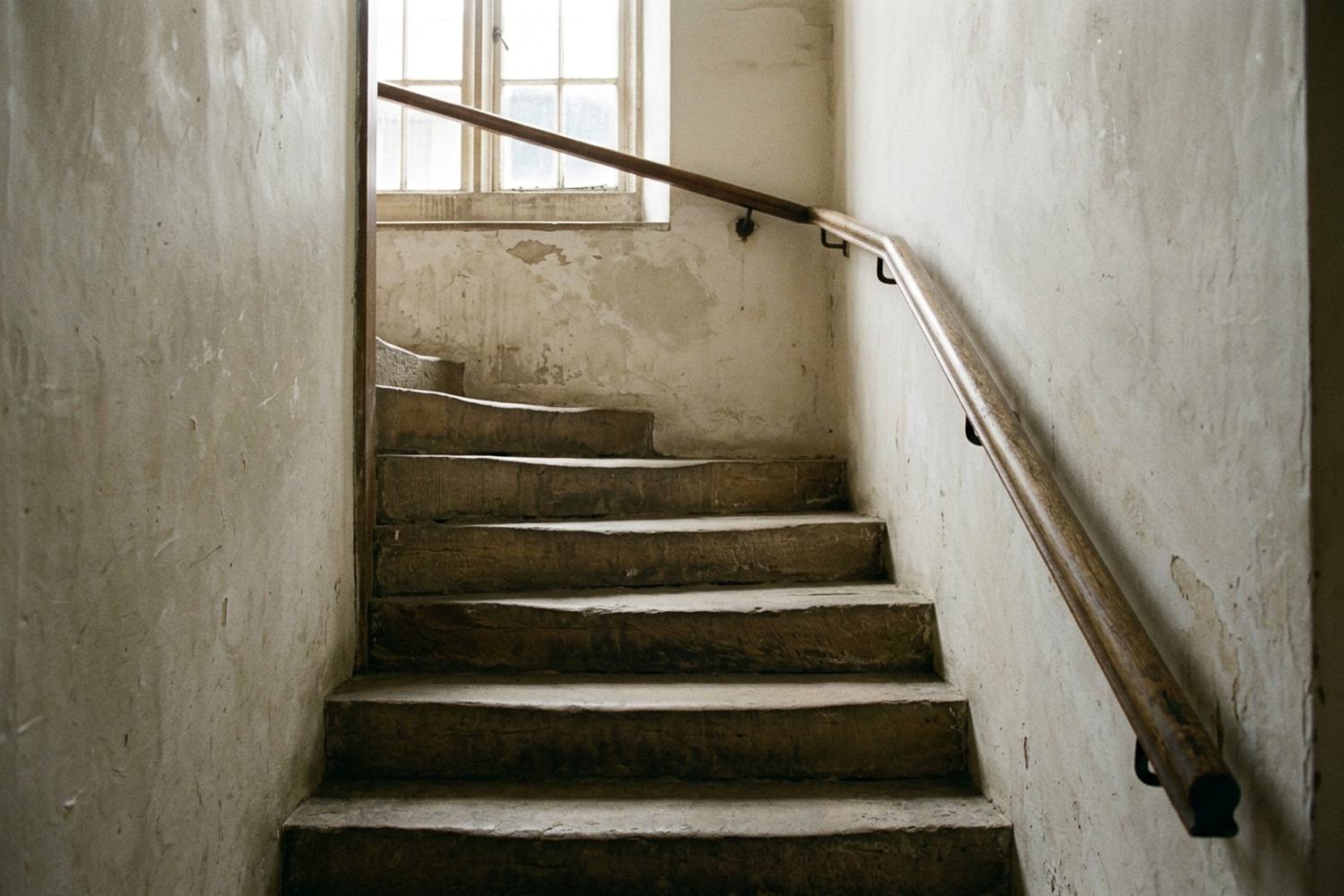 A turn in a stone staircase with daylight falling from a window above.