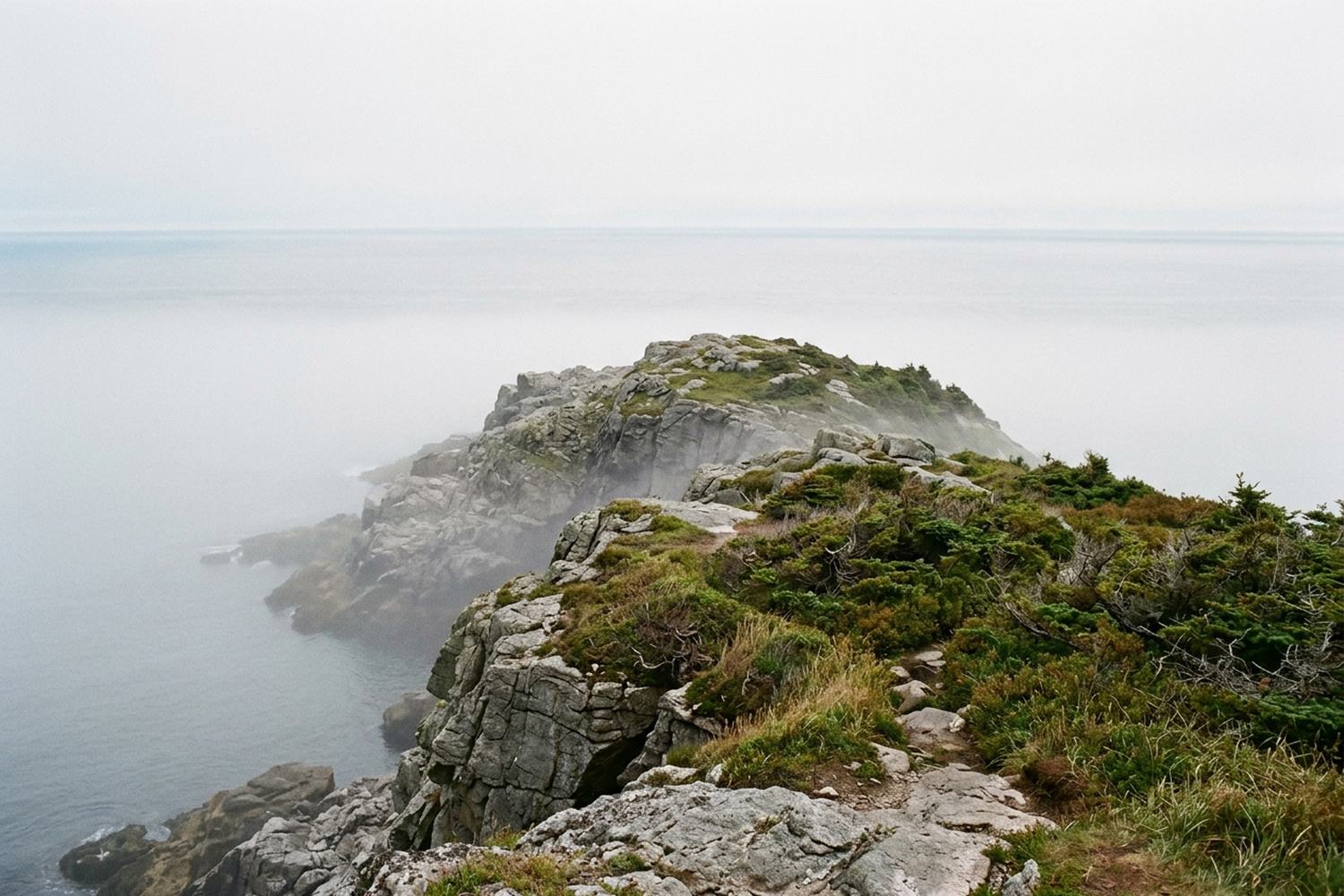 A grey rock headland above the Atlantic with fog lying on the water.